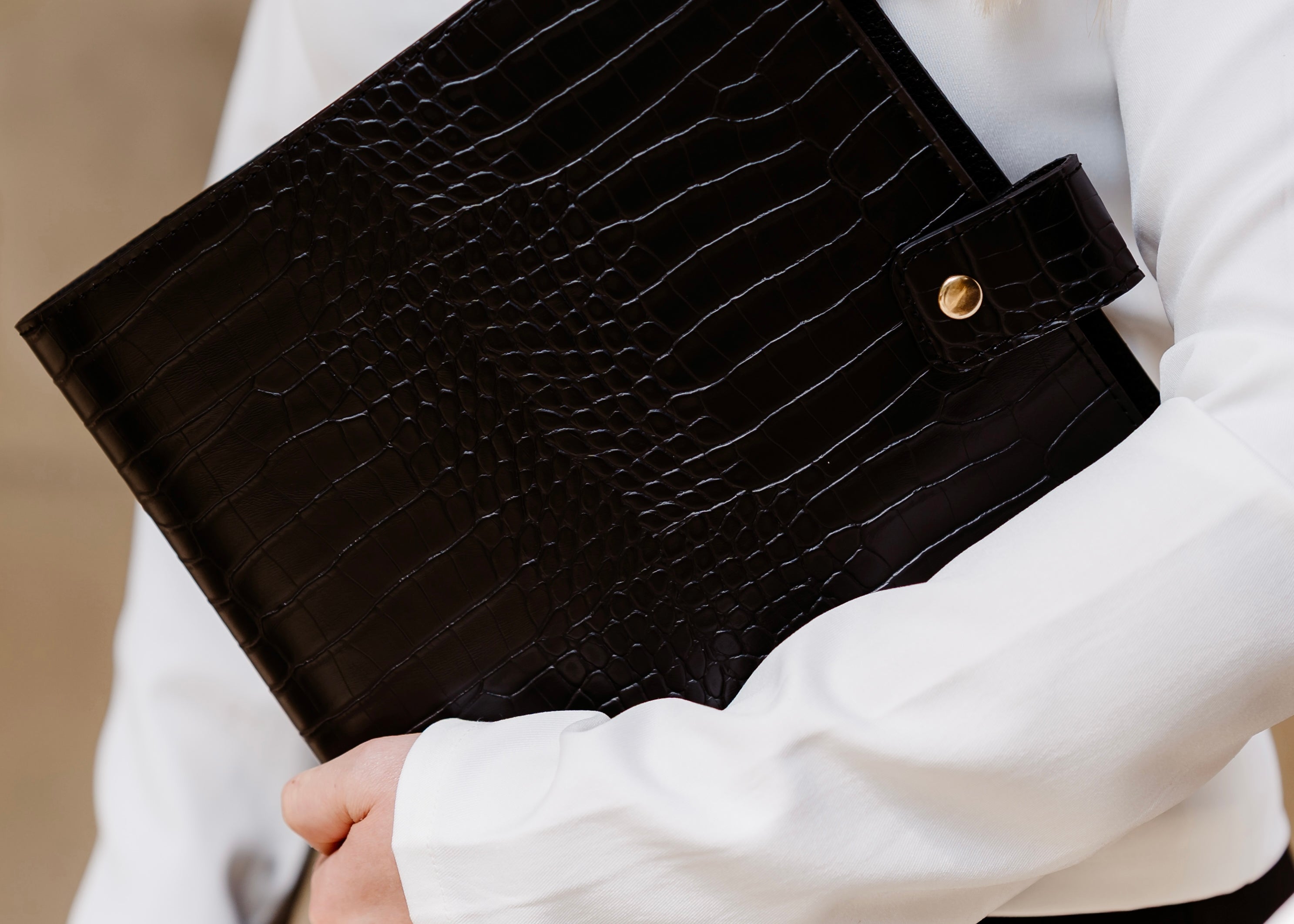 Black crocodile-patterned planner held by a person wearing a white jacket.