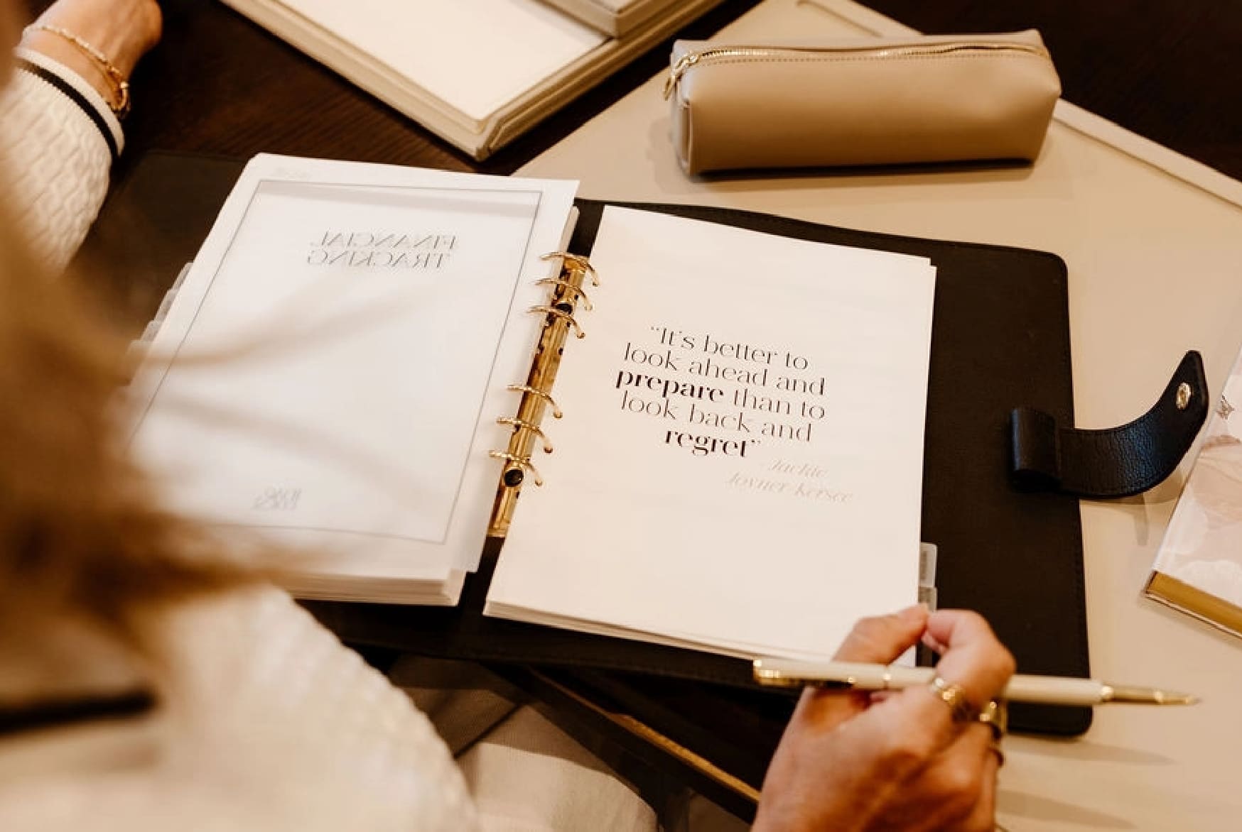 Person holding a pen over an open book with a quote on a desk.