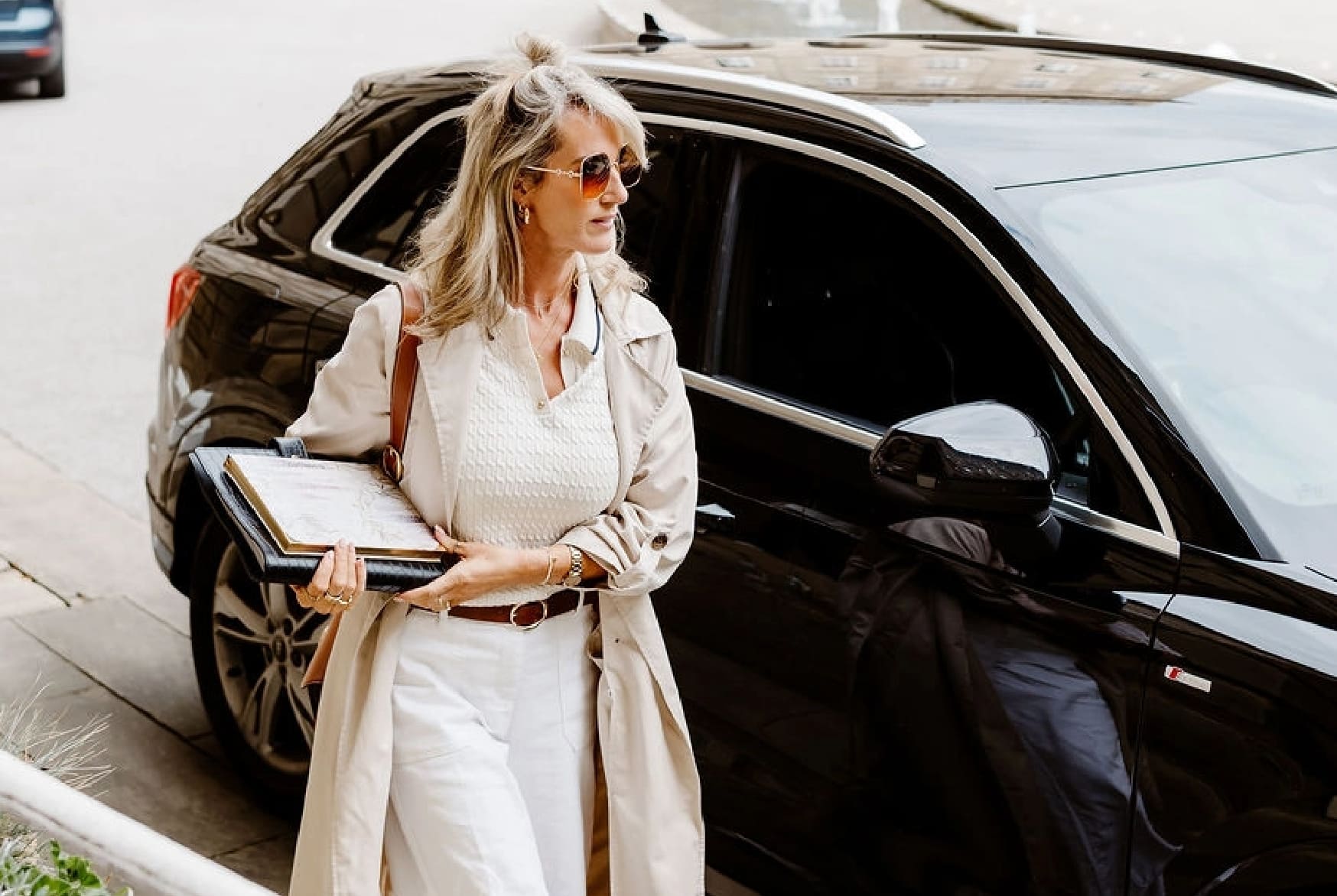 Woman in a white outfit stepping out of a black car on a city street.