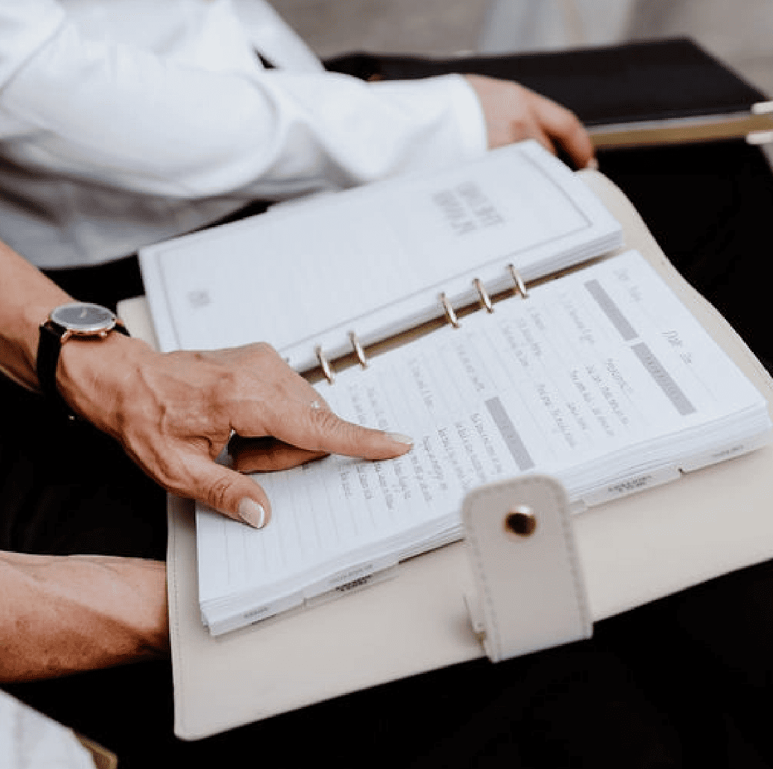 Person holding an open planner with a pen on a table
