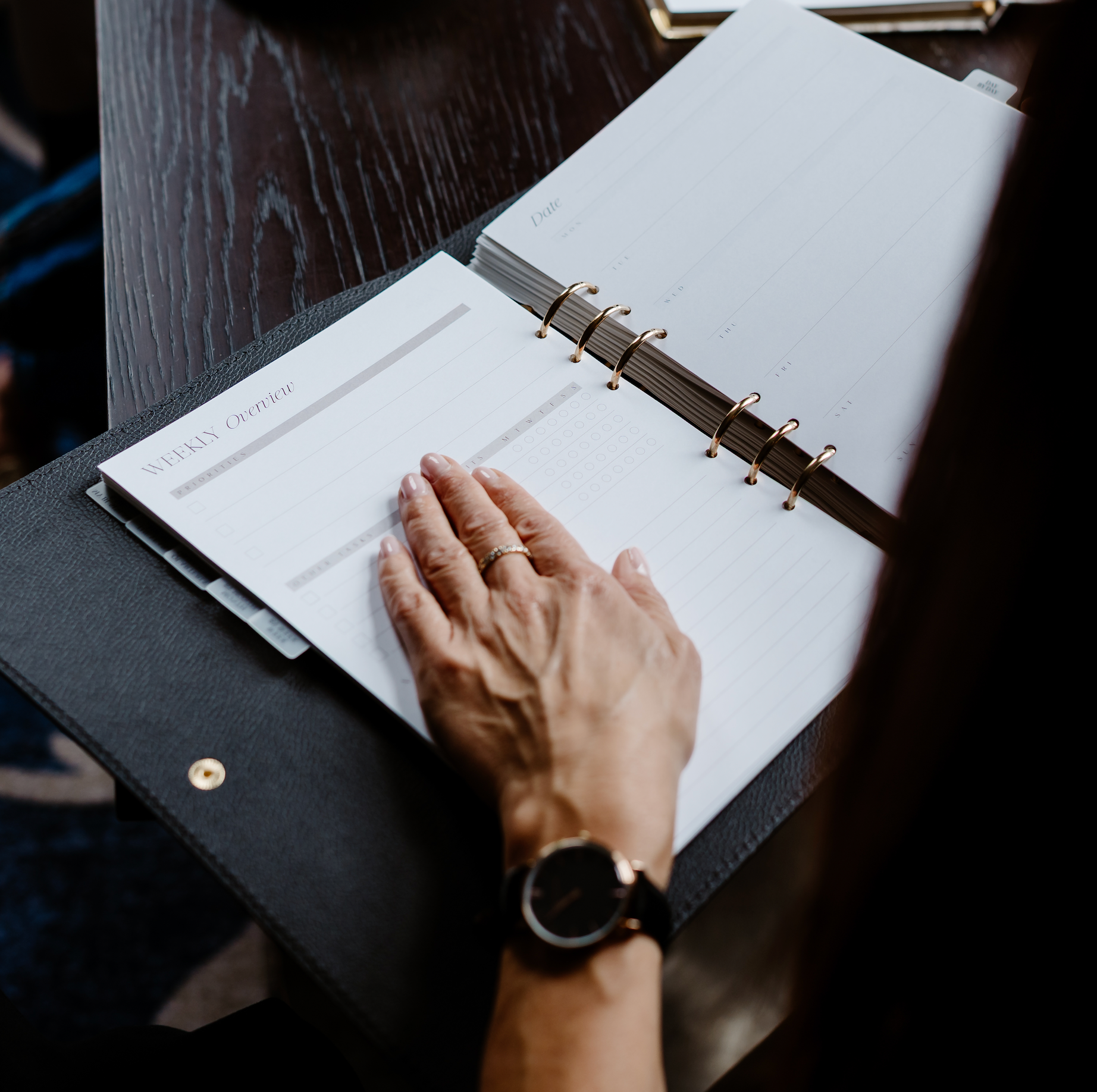 Person's hand on a planner with a dark surface underneath