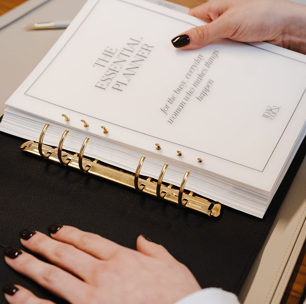 Person holding 'The Essential Planner' on a wooden surface