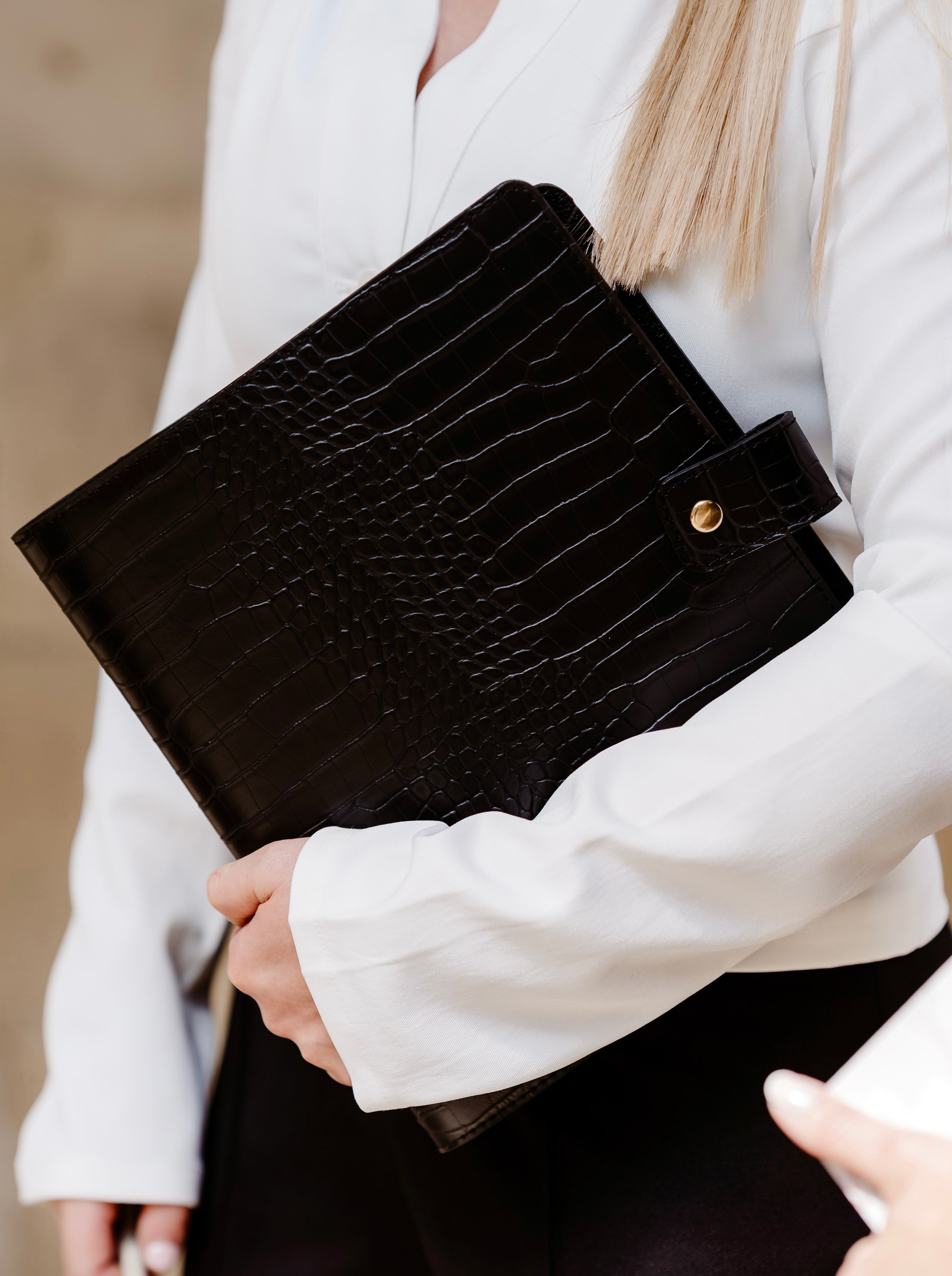 Black crocodile-patterned planner held by a person wearing a white jacket.