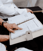 Person holding an open planner with a pen on a table