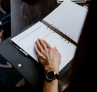 Person's hand on a planner with a dark surface underneath