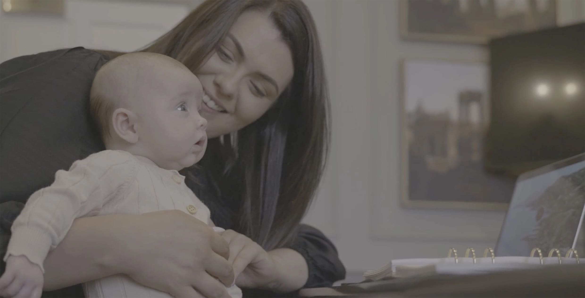 Woman holding a baby while using a laptop in a home setting